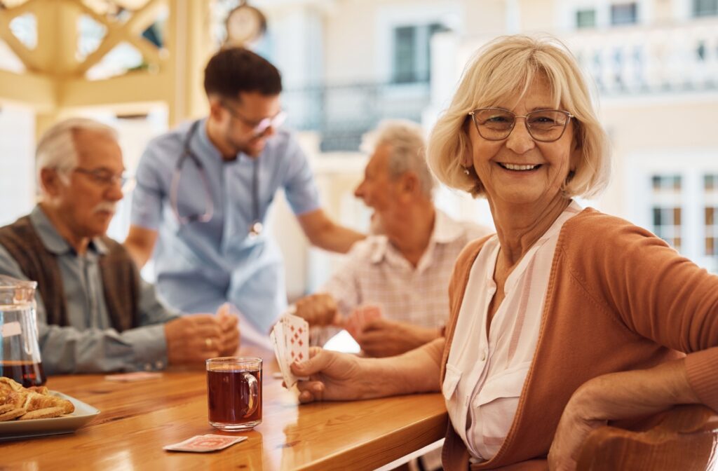 An older adult woman smiling while playing cards with a group of other residents at an assisted living community.