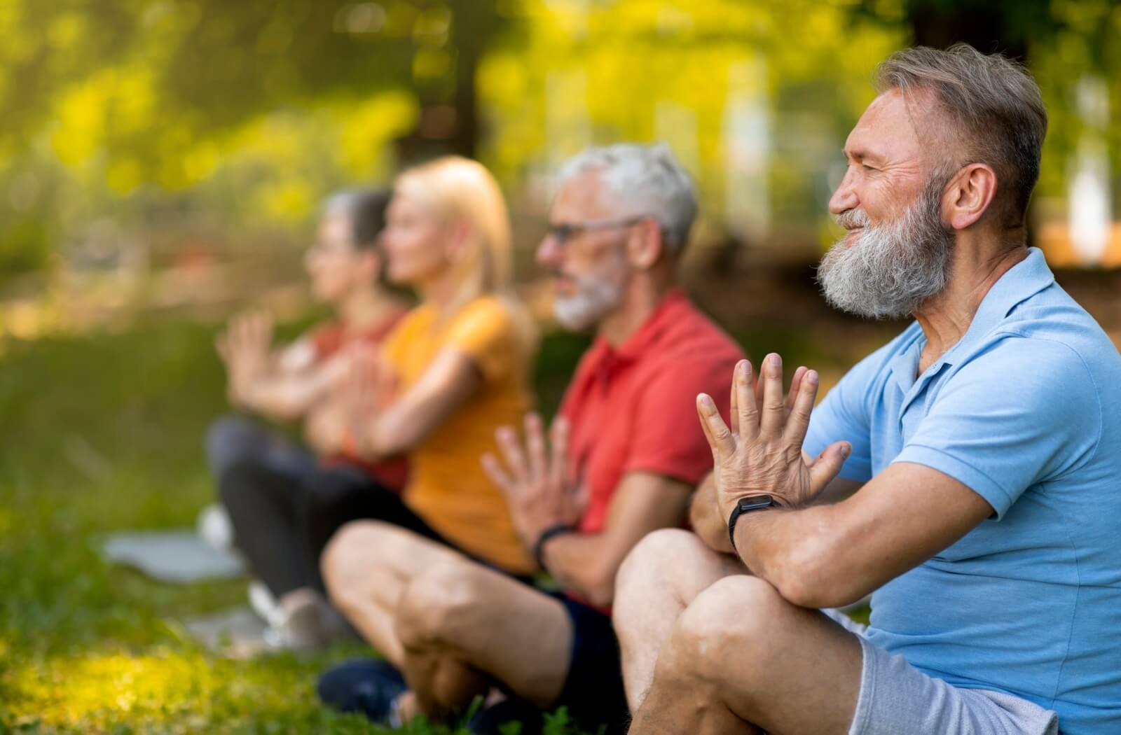 A group of focused older adults practicing meditation in a serene park.