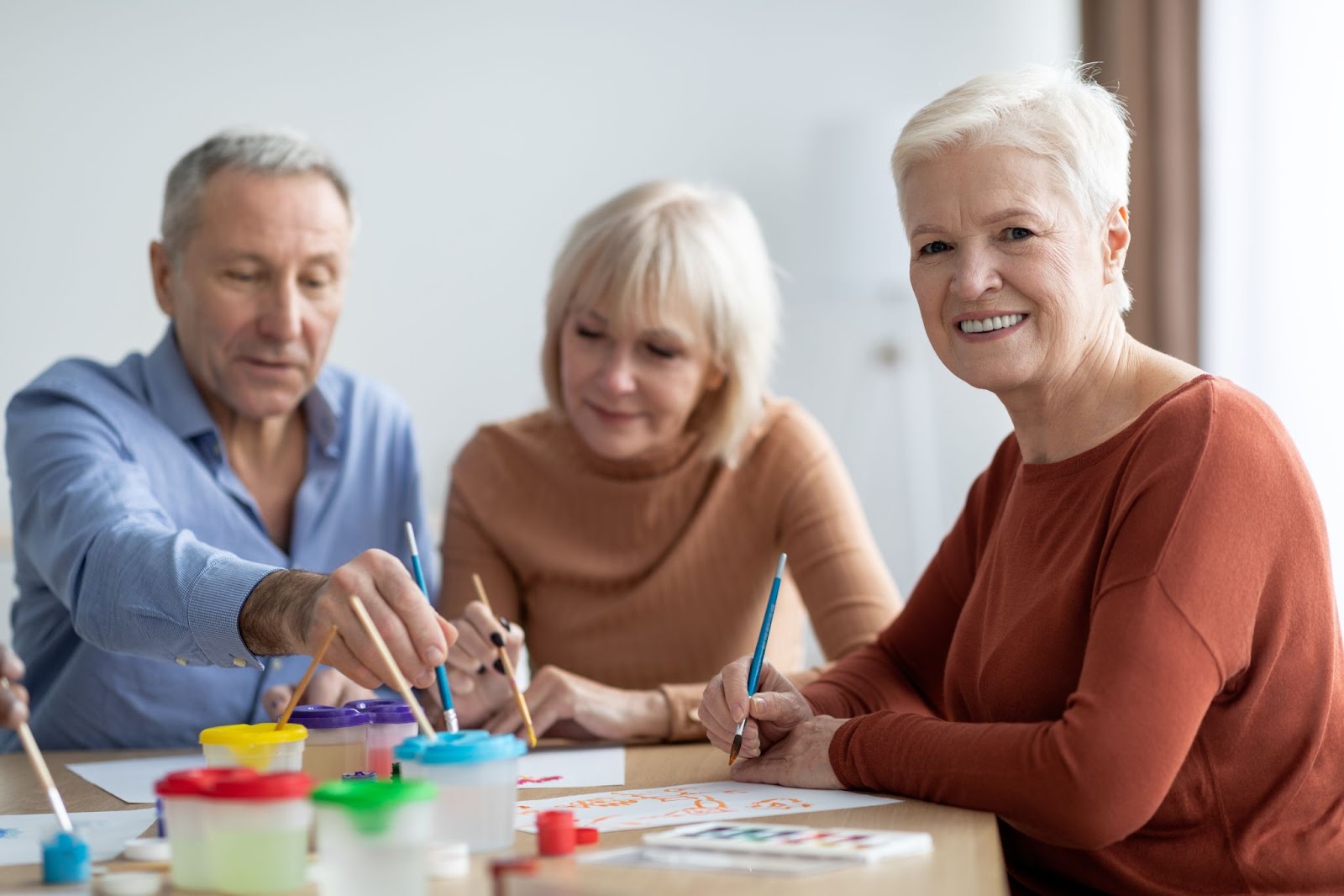 : A group of older adults enjoying painting during art therapy in a memory care community.