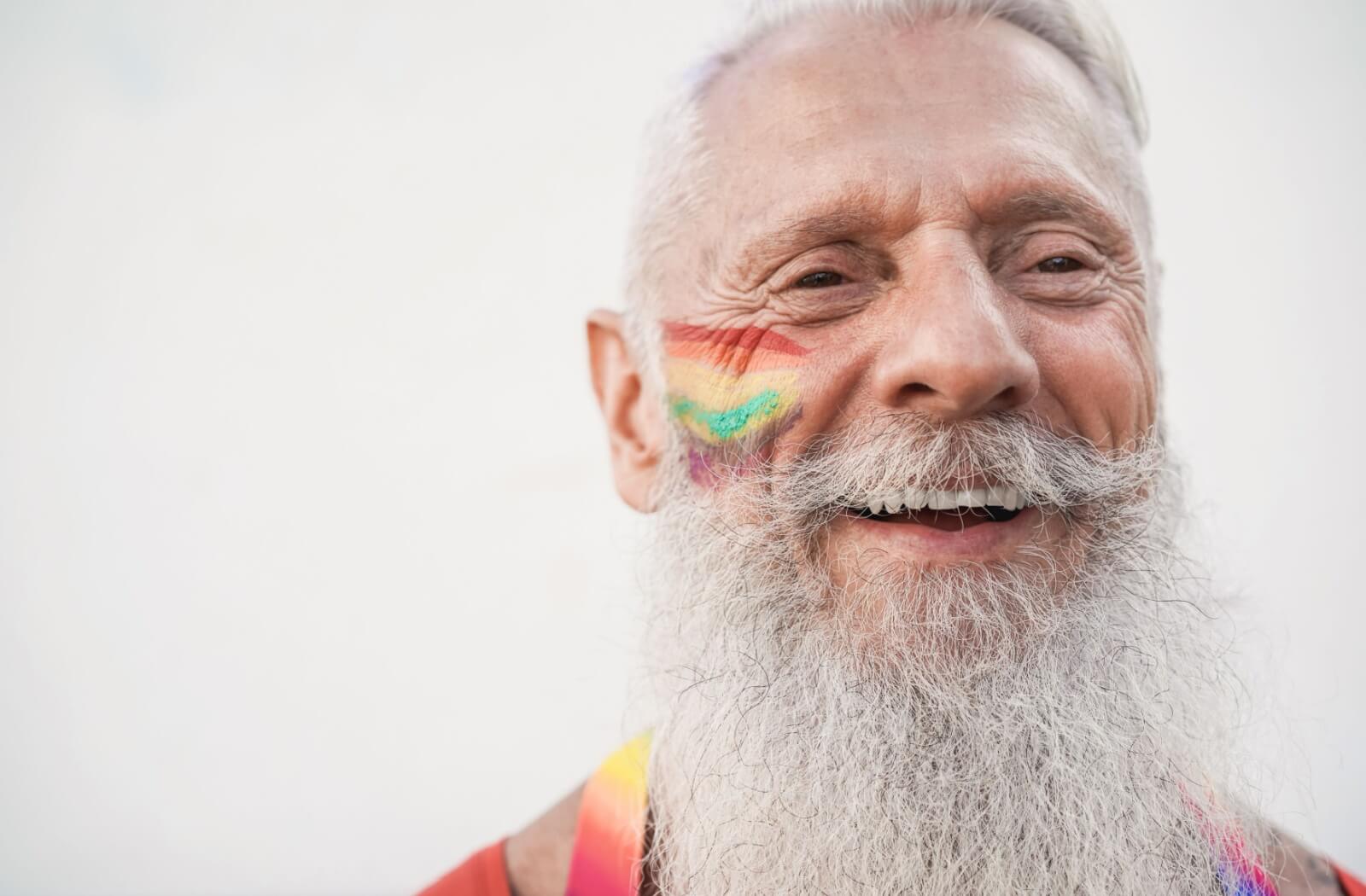 An older adult with a rainbow painted on their face smiles.