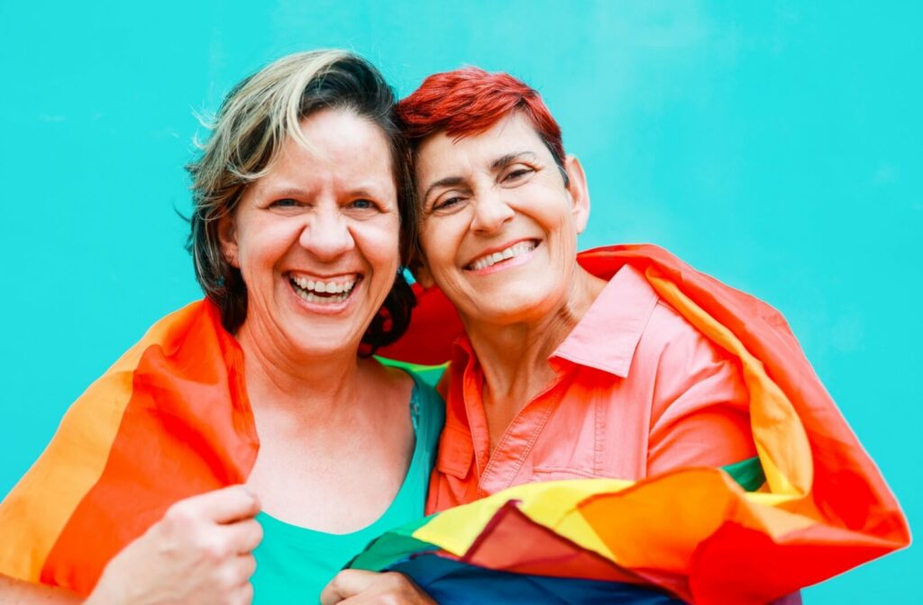 A smiling older adult couple wraps themselves in a rainbow flag.