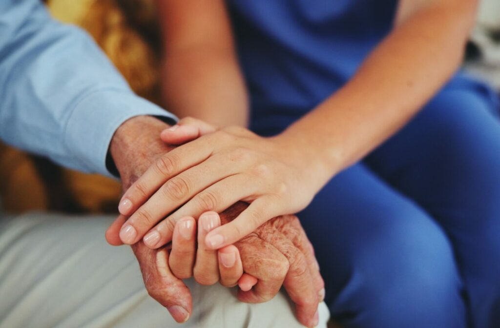 A healthcare worker holds an LGBTQ older adult's hand gently their own to show empathy and compassion for their needs.