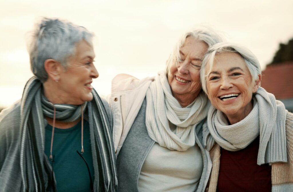 Three older adult friends smile and laugh while on an outdoor walk to see the sunset, happy to be together