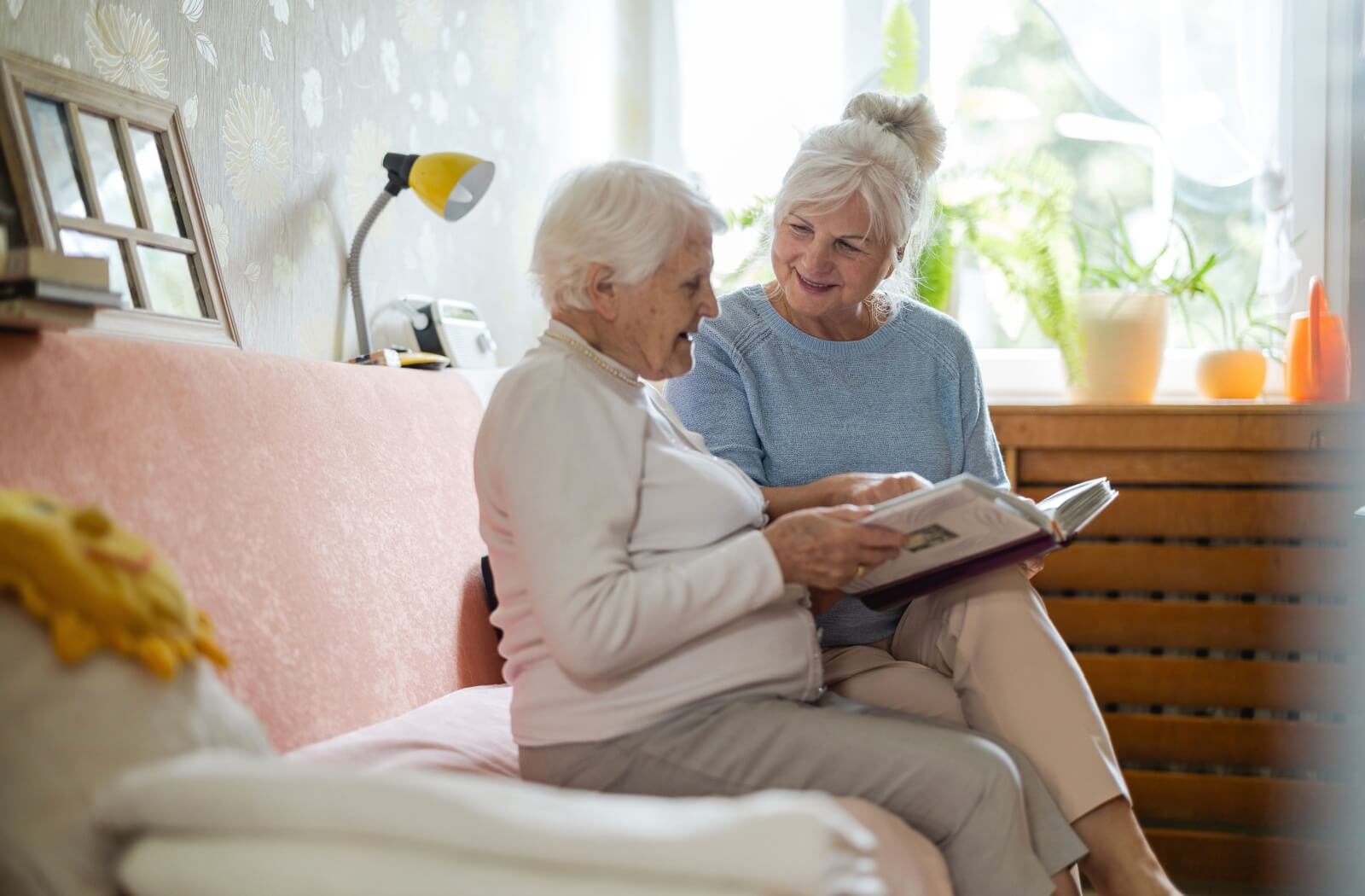 An older adult visits their older parent in memory care while they flip through a photo album together