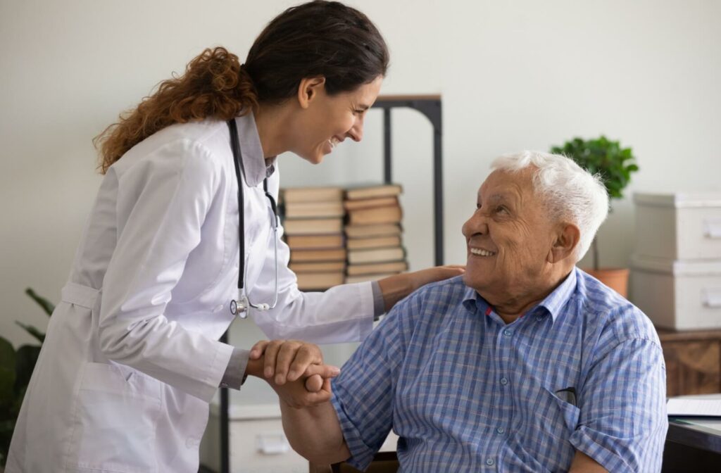 An older adult smiles as a caregiver in memory care helps them to their feet after a health checkup