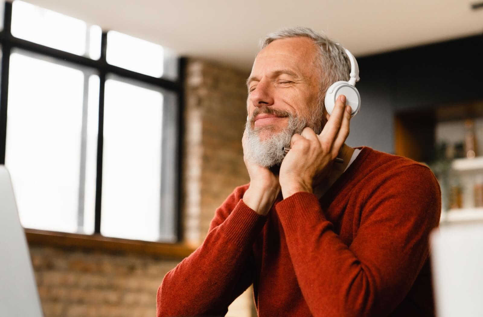 An older adult enjoys listening to music on headphones in a memory care community.