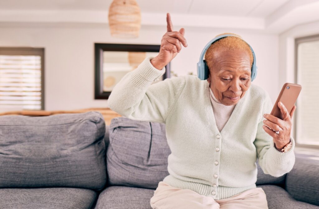 An older adult wearing headphones listens to music from their favorite playlist on their phone.