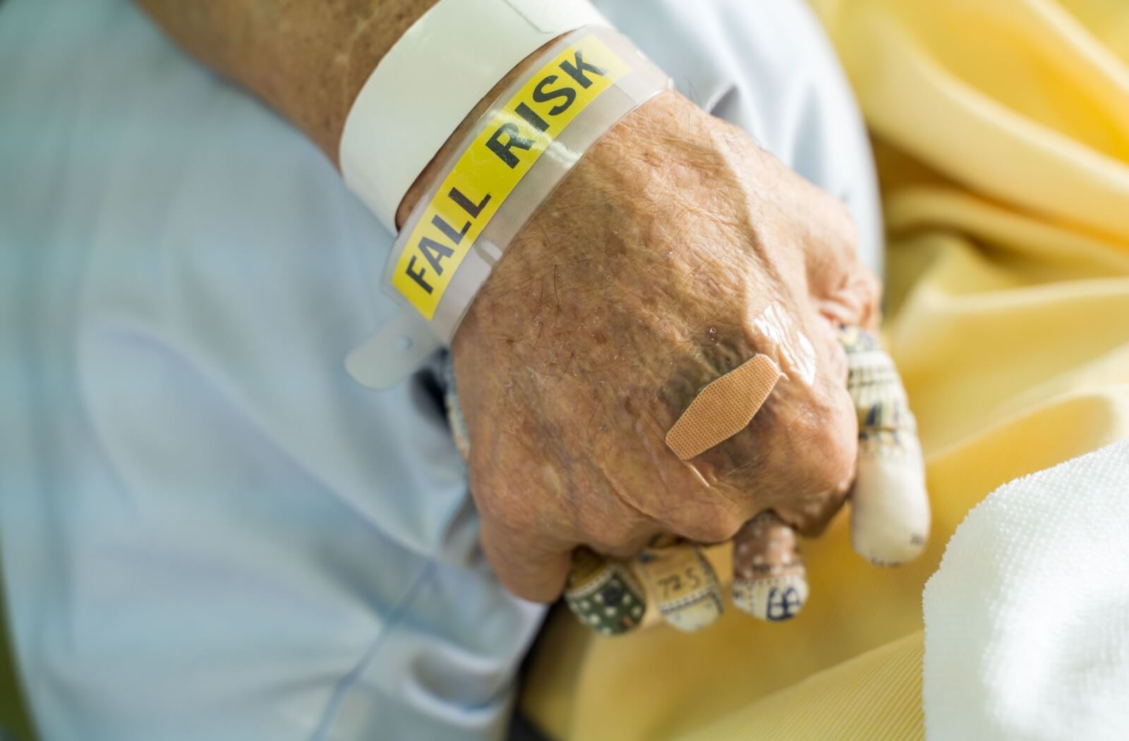 Close-up of a senior’s closed fist, with a bandaid on the knuckle and a yellow hospital “Fall Risk” wristband