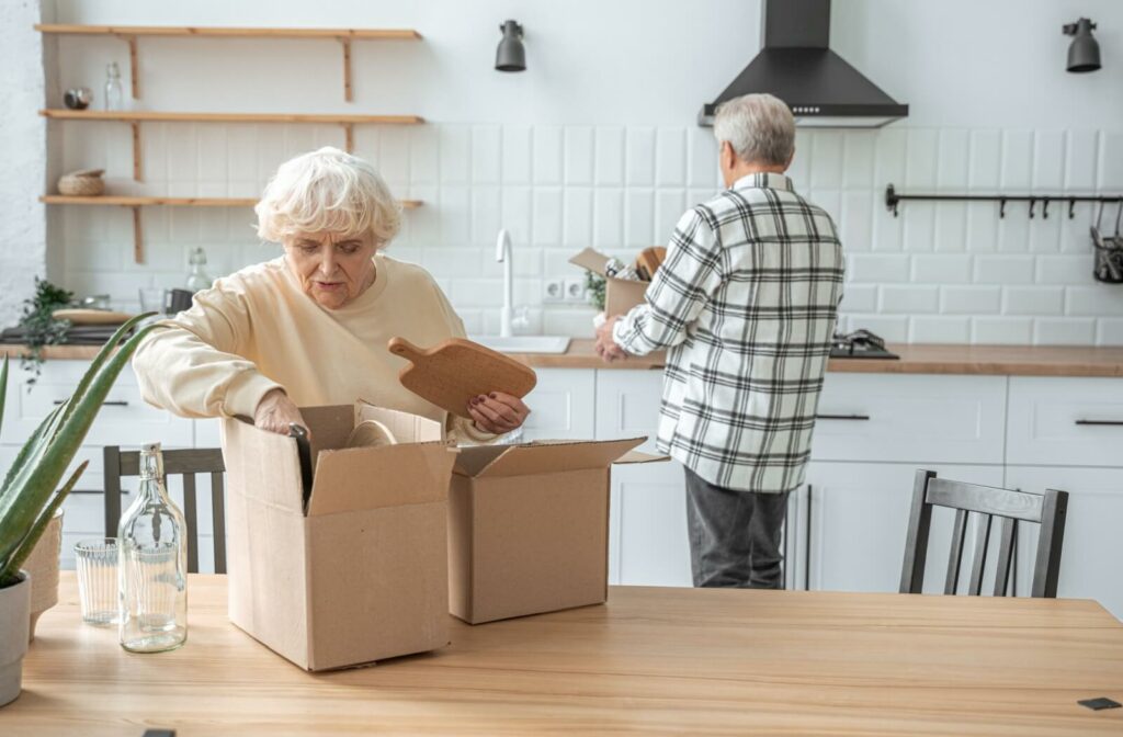 An older adult couple packs kitchen items into boxes as they downsize for a move to assisted living.